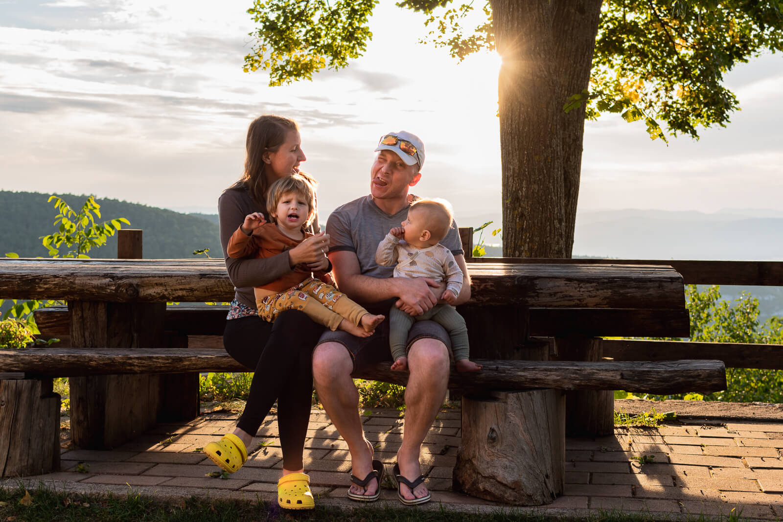 Über mich - Eine junge Familie sitzt im Sonnenuntergang auf einer Bank und albert herum